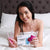 Une femme avec un kit de blanchiment des dents sur un lit. Trois seringues de gel de blanchiment dentaire et un embout buccal avec une lampe UV pour blanchir les dents.
