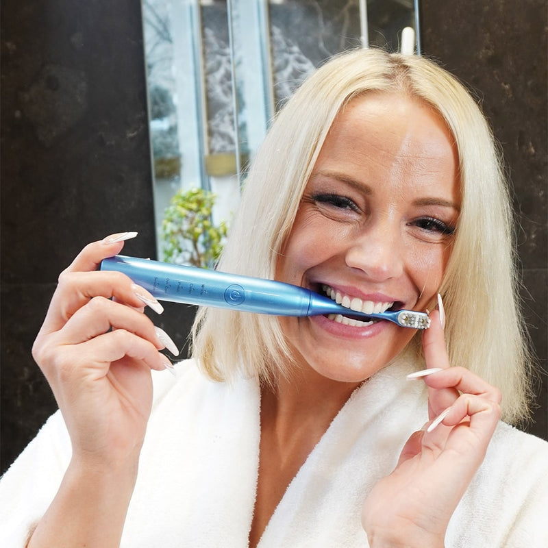 Femme avec une brosse à dents sonique Power LED Bleaching de Diamond Smile dans la bouche dans la salle de bain