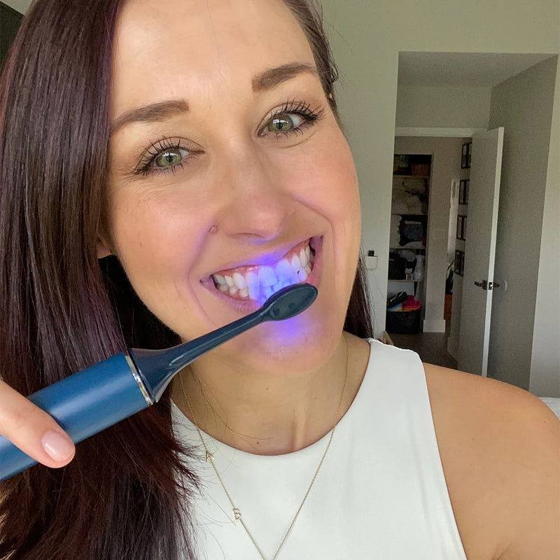 Femme se brossant les dents avec la brosse à dents sonique Power LED Bleaching de Diamond Smile dans la main