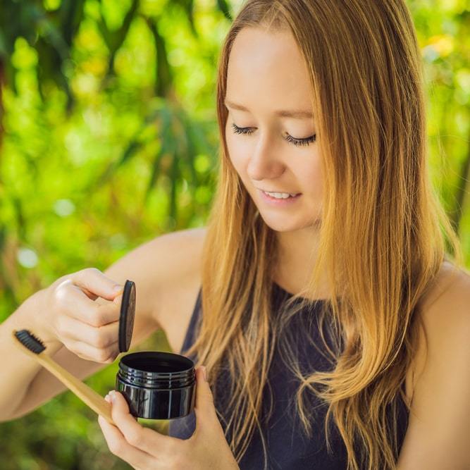 Femme avec brosse à dents et poudre de charbon actif pour le blanchiment des dents Diamond Smile Coco Powder